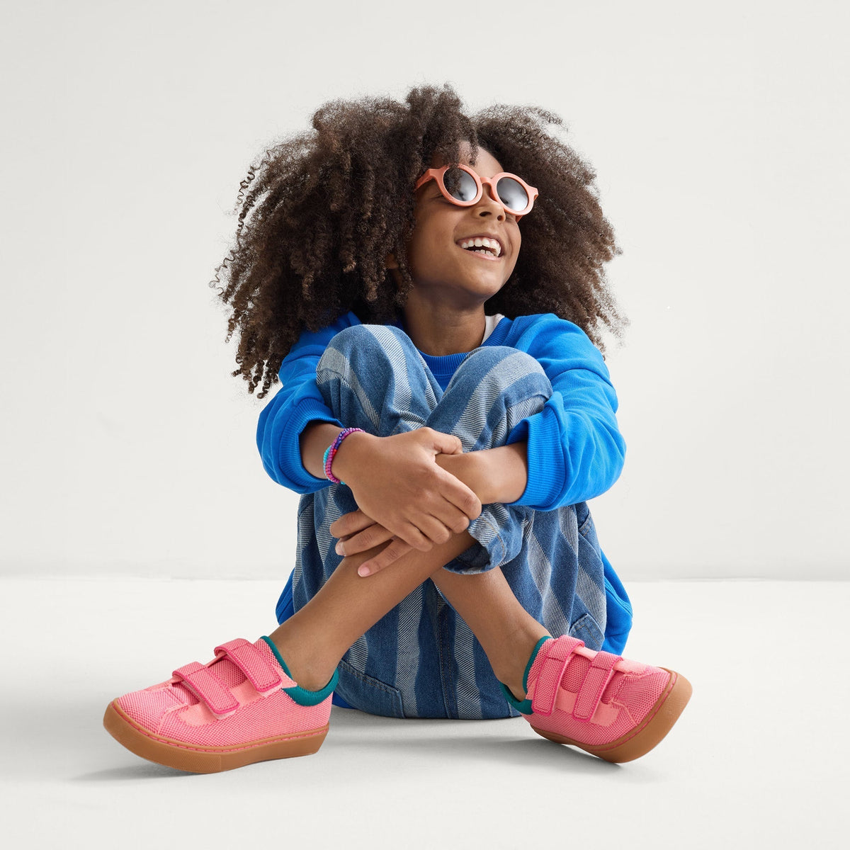 model | An alternate image of a child modeling The Kids Strap Sneaker in Watermelon.
