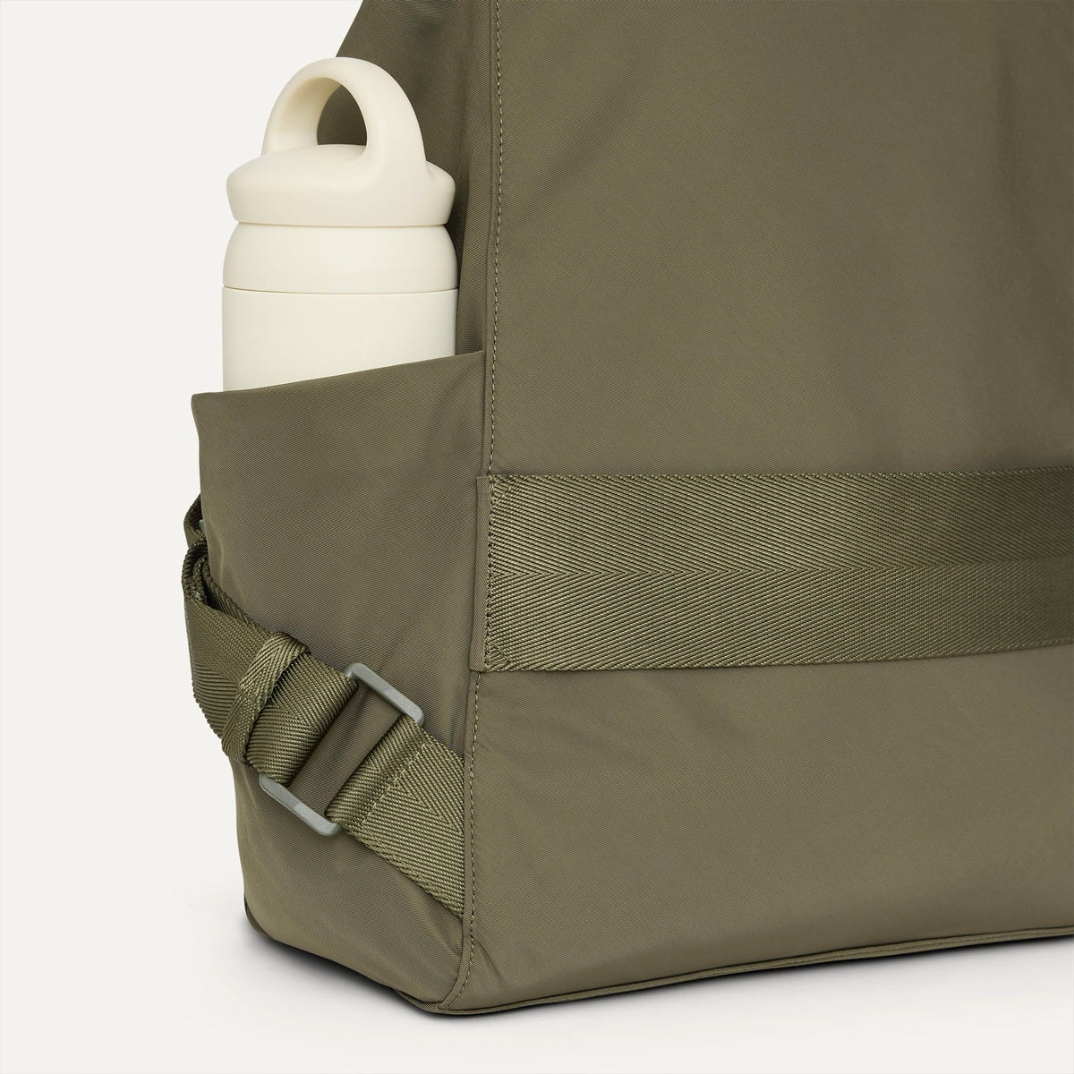 A close up of the The Travel Cinch Backpack in Forest focusing on the straps, and the side pocket.